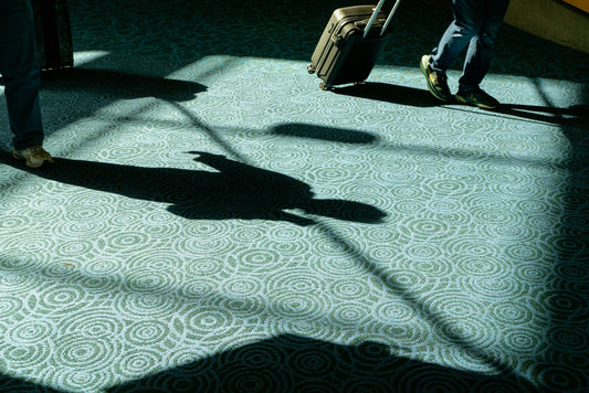 Long shadows of travelers with luggage on patterned carpet.